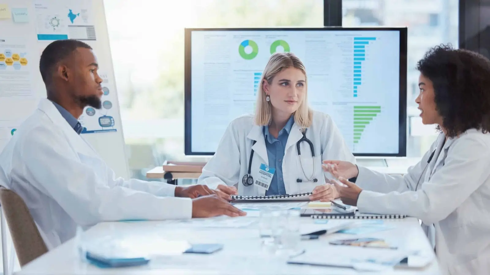 Three clinicians reviewing financial reporting around a table, a dashboard on the screen behind them